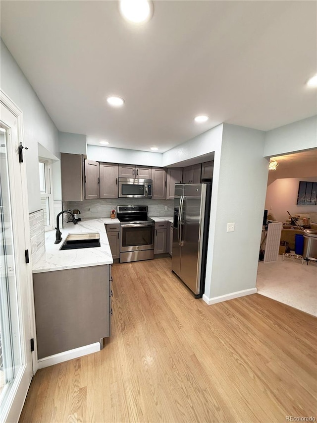 kitchen featuring stainless steel appliances, light stone counters, light hardwood / wood-style floors, and sink