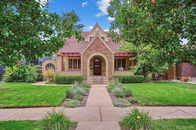 tudor home with a shingled roof, a front yard, and brick siding