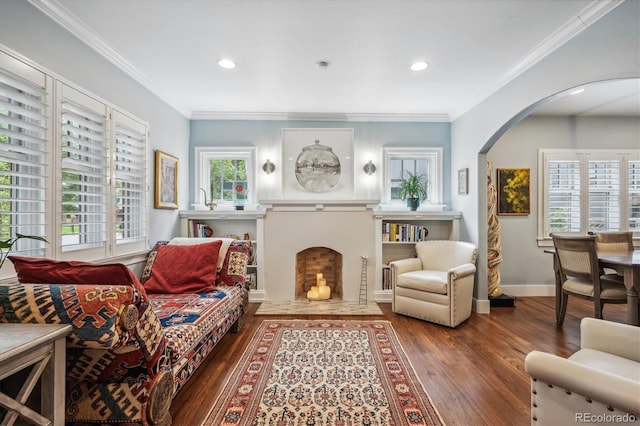 living area with a fireplace with flush hearth, arched walkways, wood finished floors, and ornamental molding