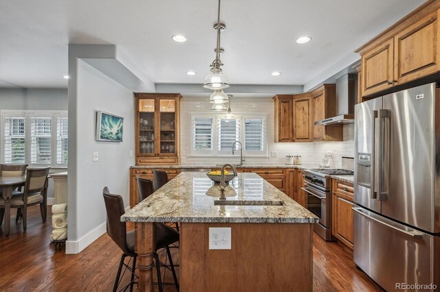 kitchen with a kitchen breakfast bar, a healthy amount of sunlight, appliances with stainless steel finishes, wall chimney range hood, and brown cabinets