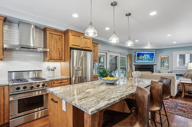 kitchen featuring dark wood-style flooring, a fireplace, appliances with stainless steel finishes, open floor plan, and wall chimney exhaust hood