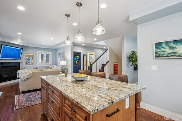 kitchen with dark wood-style floors, brown cabinetry, a glass covered fireplace, open floor plan, and light stone countertops