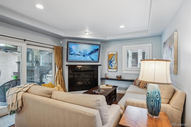 living room featuring a glass covered fireplace, wood finished floors, a tray ceiling, and recessed lighting