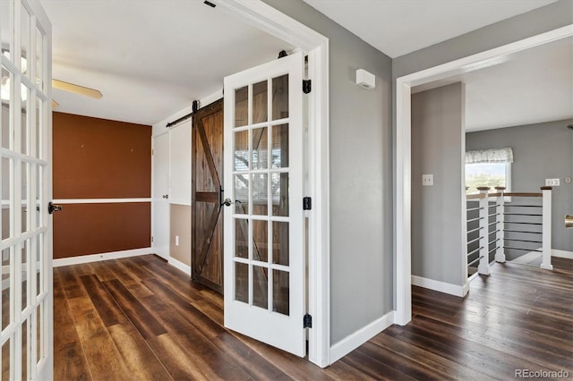 corridor with a barn door, dark hardwood / wood-style flooring, and french doors