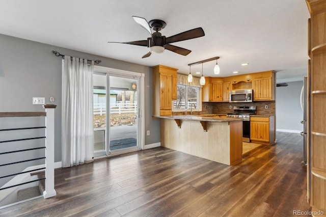 kitchen featuring hanging light fixtures, kitchen peninsula, a kitchen bar, decorative backsplash, and appliances with stainless steel finishes