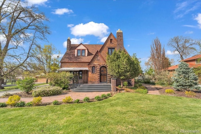tudor-style house with brick siding, a chimney, and a front lawn
