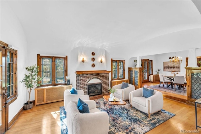 living room with an inviting chandelier, a brick fireplace, plenty of natural light, and wood finished floors
