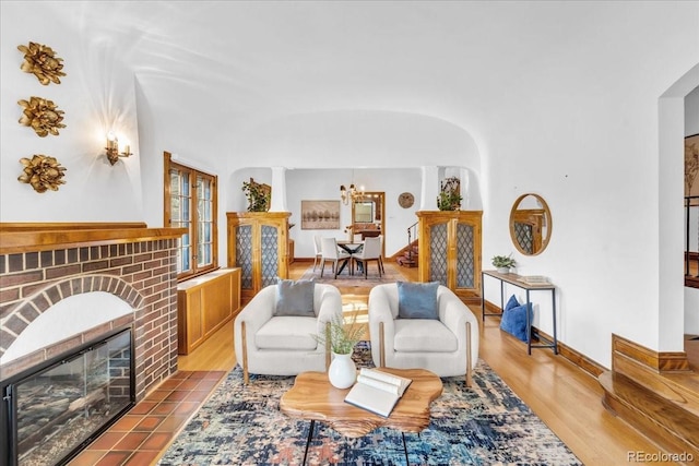 living room with a brick fireplace, arched walkways, a notable chandelier, and wood finished floors