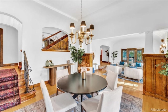 dining space featuring an inviting chandelier, stairs, wood finished floors, arched walkways, and vaulted ceiling