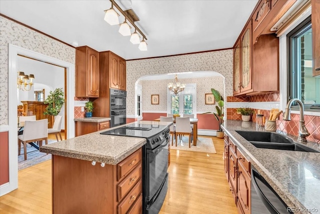kitchen with arched walkways, a sink, black appliances, a notable chandelier, and wallpapered walls