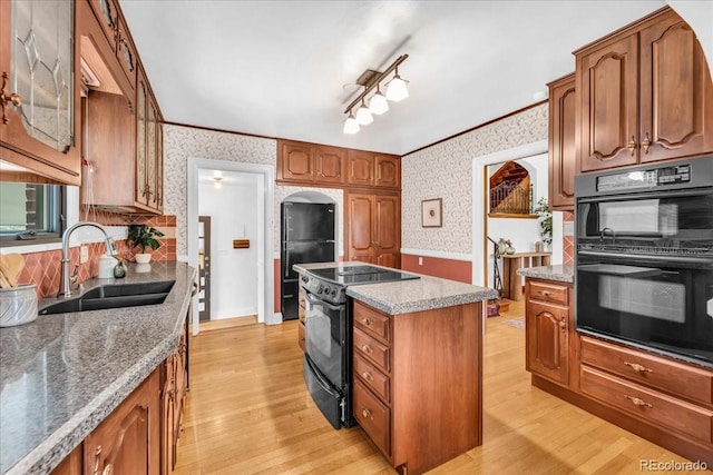 kitchen with a kitchen island, wallpapered walls, a sink, light wood-style flooring, and black appliances