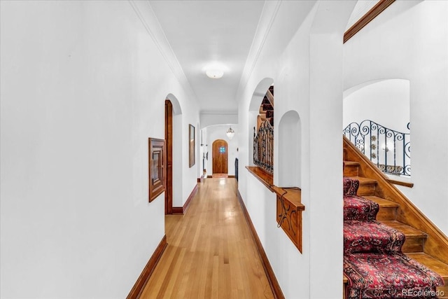 corridor with light wood finished floors, arched walkways, stairs, baseboards, and ornamental molding