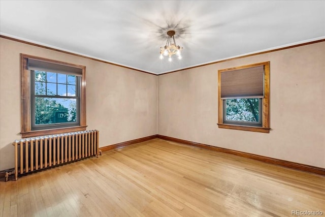 spare room featuring crown molding, wood-type flooring, a chandelier, radiator, and baseboards