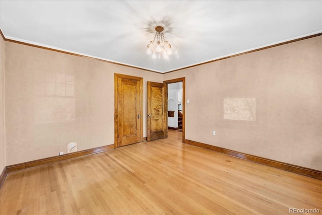 empty room featuring baseboards, a notable chandelier, ornamental molding, and wood finished floors