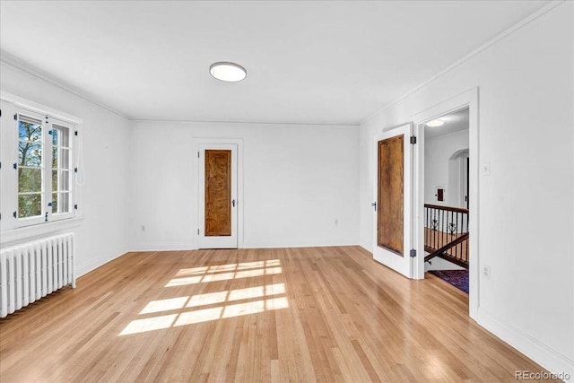 unfurnished room featuring radiator heating unit, baseboards, ornamental molding, and light wood-type flooring