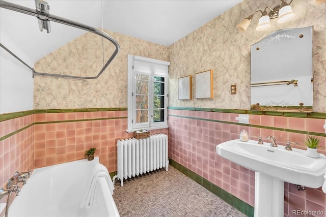 bathroom with a bath, radiator, wainscoting, and tile walls