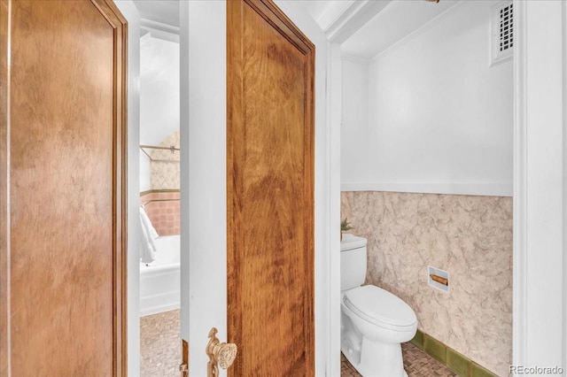 bathroom featuring wainscoting, toilet, a bathtub, visible vents, and ornamental molding