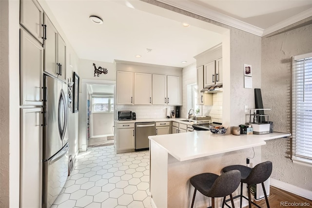 kitchen with sink, kitchen peninsula, a breakfast bar area, appliances with stainless steel finishes, and ornamental molding