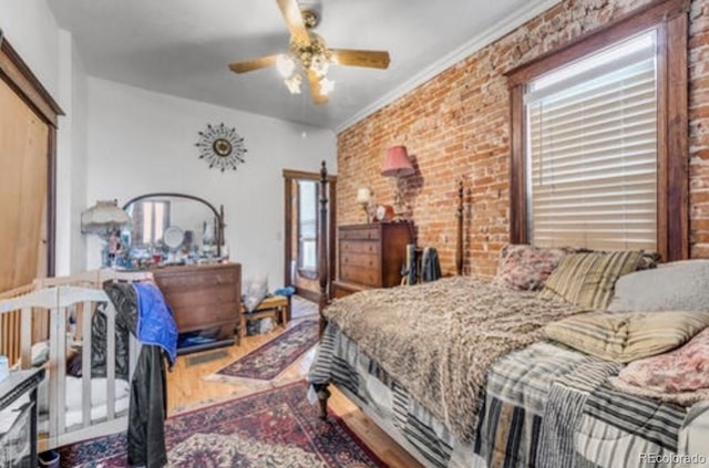 bedroom with hardwood / wood-style flooring, ornamental molding, ceiling fan, and brick wall