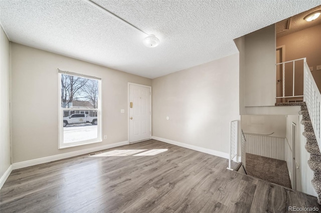 foyer with stairway, a textured ceiling, baseboards, and wood finished floors