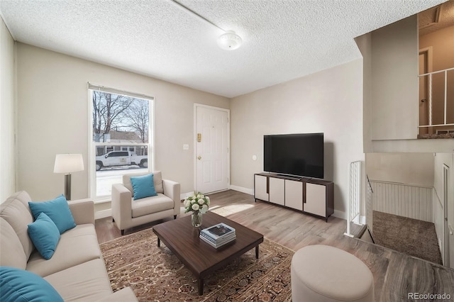 living room with baseboards, a textured ceiling, and light wood finished floors