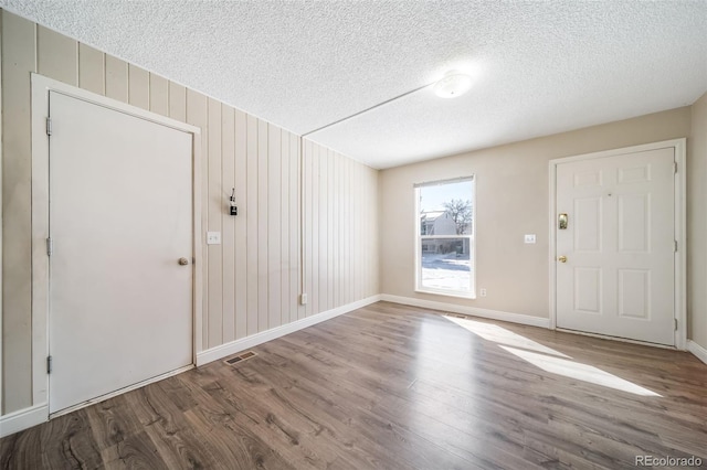 foyer entrance with baseboards, a textured ceiling, visible vents, and wood finished floors