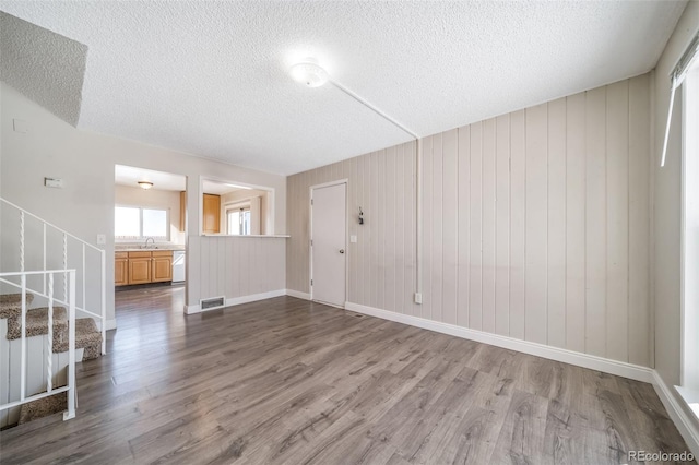 empty room featuring a sink, wood finished floors, visible vents, stairs, and baseboards