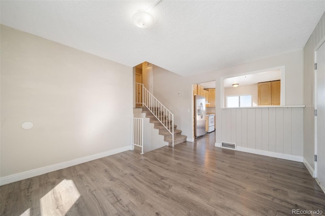 interior space with visible vents, a textured ceiling, wood finished floors, baseboards, and stairs