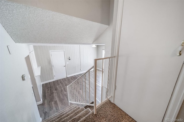 stairway featuring lofted ceiling, a textured ceiling, and wood finished floors