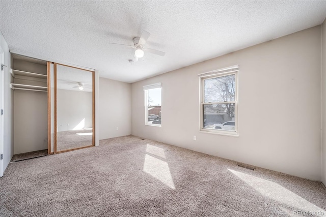 unfurnished bedroom featuring a textured ceiling, carpet floors, visible vents, a ceiling fan, and a closet