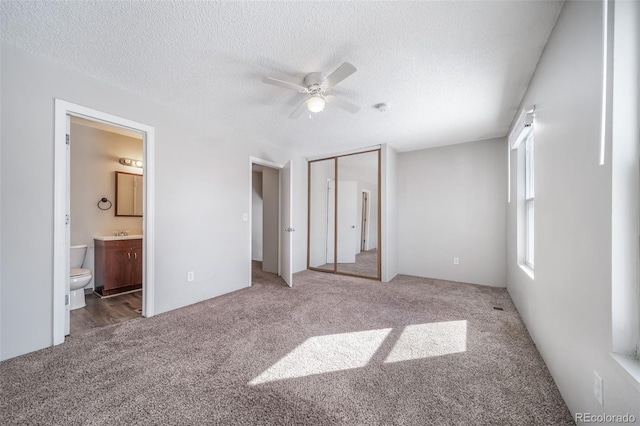 unfurnished bedroom with ensuite bath, a closet, a textured ceiling, and carpet flooring