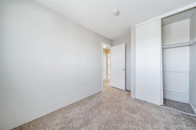 unfurnished bedroom with light carpet, a textured ceiling, and a closet