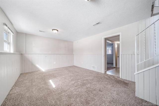 empty room featuring a healthy amount of sunlight, visible vents, and a wainscoted wall