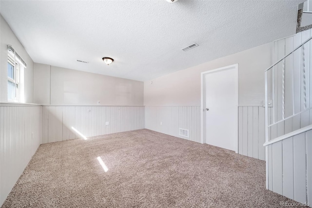 carpeted empty room featuring wainscoting, visible vents, and a textured ceiling