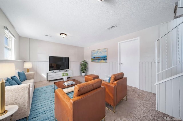 living room with a wainscoted wall, a textured ceiling, visible vents, and carpet flooring