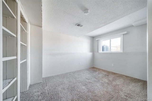 unfurnished room with carpet, visible vents, and a textured ceiling