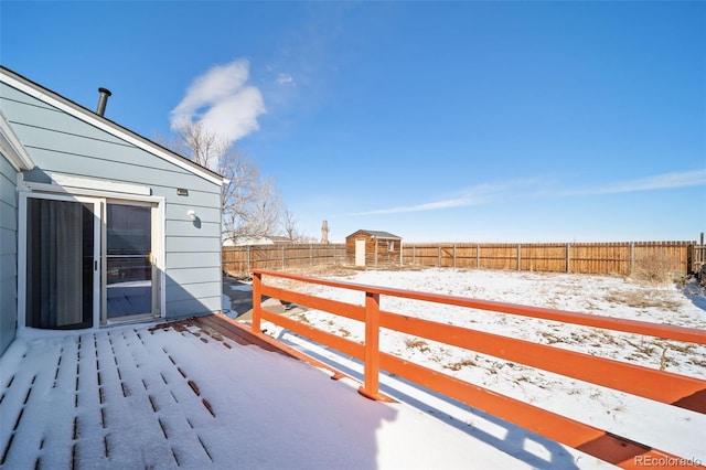 snow covered deck featuring an outbuilding, a storage unit, and a fenced backyard