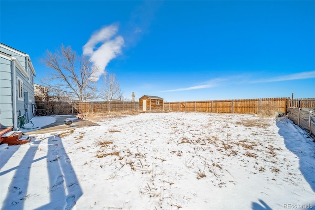 yard layered in snow featuring a fenced backyard, an outdoor structure, and a shed