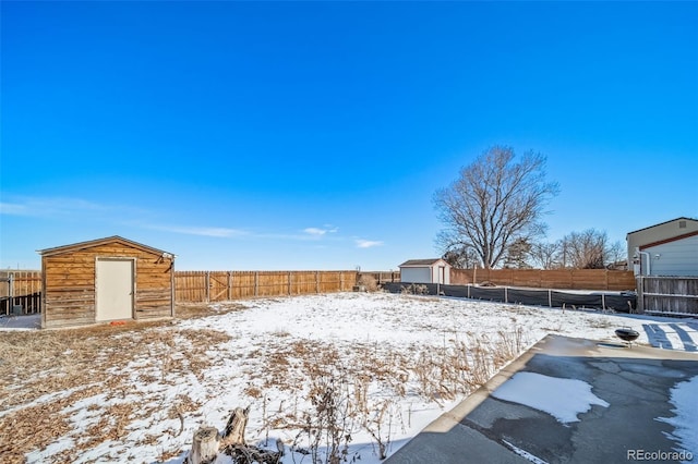 snowy yard featuring a fenced backyard, a shed, and an outbuilding