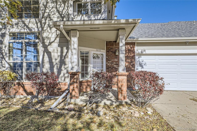 view of exterior entry featuring a garage, brick siding, and roof with shingles