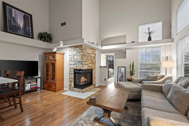 living room featuring a stone fireplace, a high ceiling, visible vents, and wood finished floors