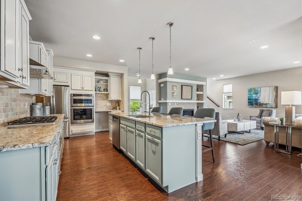 kitchen with appliances with stainless steel finishes, a kitchen island with sink, sink, pendant lighting, and dark hardwood / wood-style floors