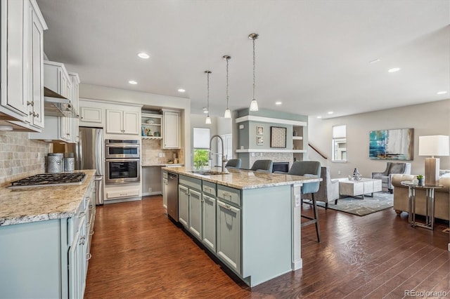 kitchen with appliances with stainless steel finishes, a kitchen island with sink, sink, pendant lighting, and dark hardwood / wood-style floors