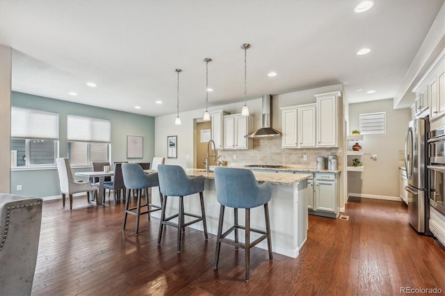 kitchen with dark hardwood / wood-style flooring, a center island with sink, hanging light fixtures, and wall chimney range hood