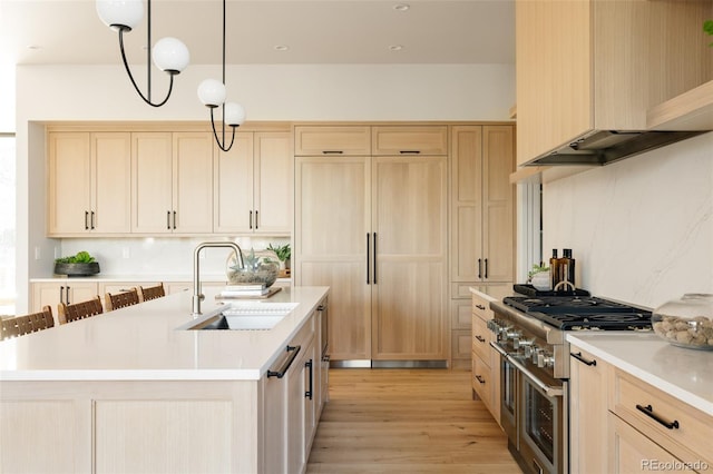 kitchen with double oven range, sink, light brown cabinetry, decorative light fixtures, and light hardwood / wood-style floors