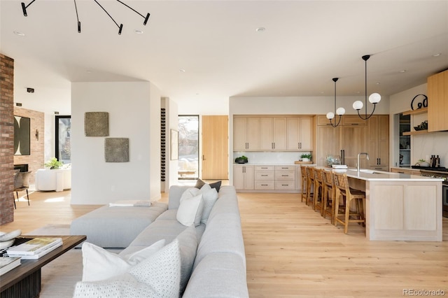 living room featuring a brick fireplace, an inviting chandelier, light hardwood / wood-style flooring, and sink