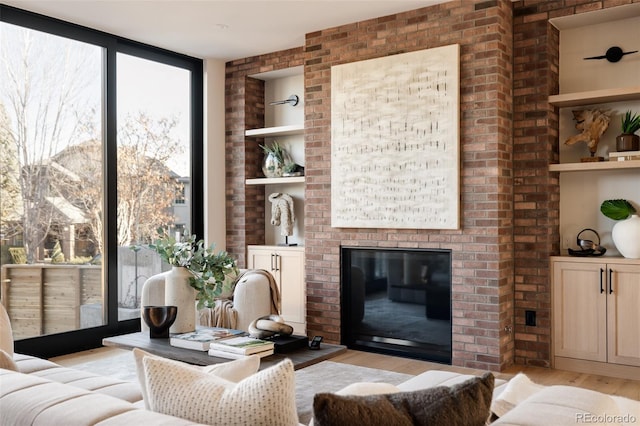 living room featuring a fireplace, built in shelves, light hardwood / wood-style flooring, and floor to ceiling windows