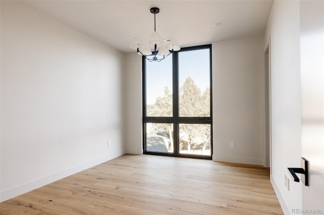 spare room with light hardwood / wood-style flooring, expansive windows, a healthy amount of sunlight, and an inviting chandelier