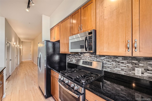 kitchen featuring dark stone counters, appliances with stainless steel finishes, brown cabinets, light wood-style floors, and backsplash