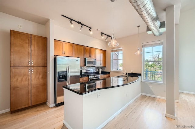 kitchen with stainless steel appliances, dark countertops, brown cabinets, and pendant lighting